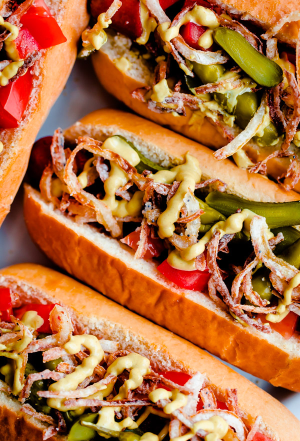 Fancy Chicago-Style Hot Dogs topped with celery salt fried onions, Dijon mustard, cornichon, spicy sport peppers, and chopped tomato! Insanely delicious and easy tailgating food.