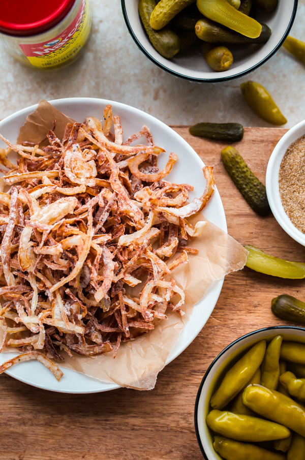 Fancy Chicago-Style Hot Dogs topped with celery salt fried onions, Dijon mustard, cornichon, spicy sport peppers, and chopped tomato! Insanely delicious and easy tailgating food.