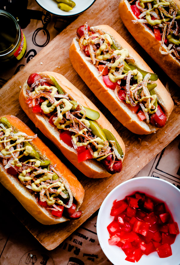 Fancy Chicago-Style Hot Dogs topped with celery salt fried onions, Dijon mustard, cornichon, spicy sport peppers, and chopped tomato! Insanely delicious and easy tailgating food.