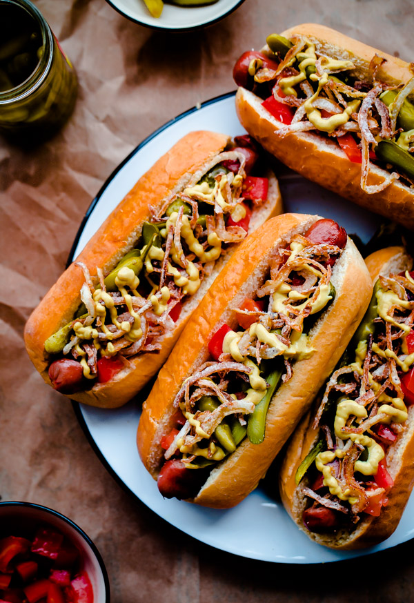 Fancy Chicago-Style Hot Dogs topped with celery salt fried onions, Dijon mustard, cornichon, spicy sport peppers, and chopped tomato! Insanely delicious and easy tailgating food.