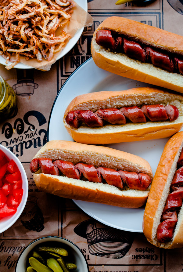 Fancy Chicago-Style Hot Dogs topped with celery salt fried onions, Dijon mustard, cornichon, spicy sport peppers, and chopped tomato! Insanely delicious and easy tailgating food.