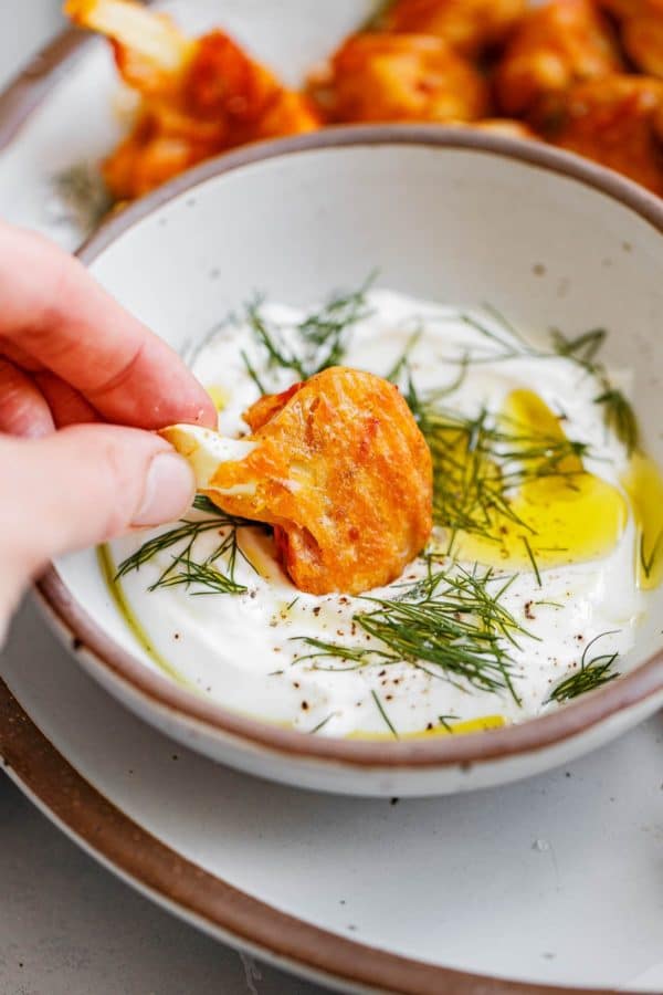 Hand Dipping Buffalo Cauliflower into Yogurt Sauce